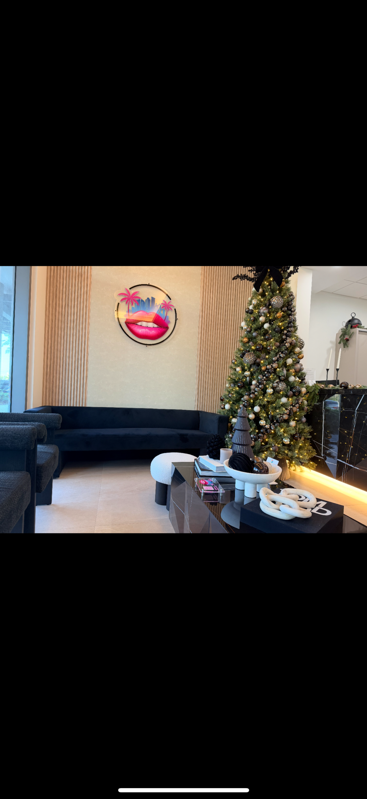 A chic Miami dental office lobby with a black sofa, festive tree, art of lips, reflecting smile makeovers and veneers.